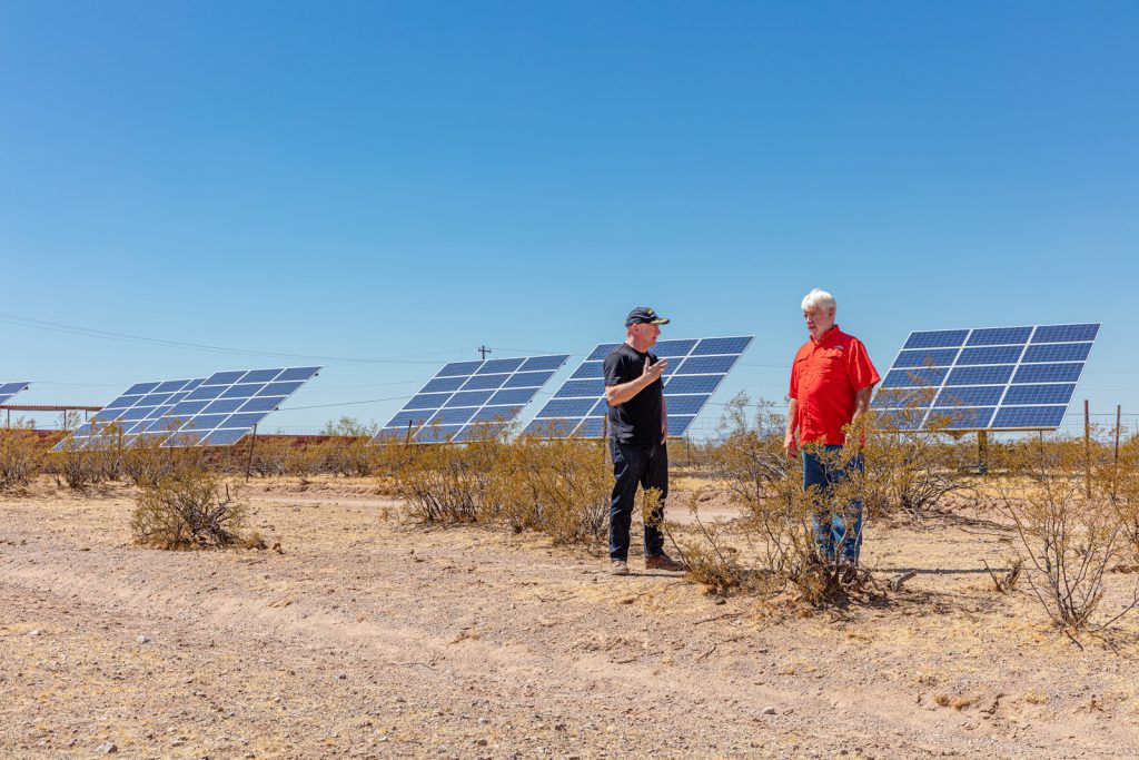 Mark Kelly stands in a field with a local technician surrounded by solar panels.